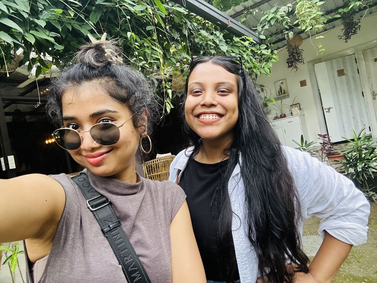 Karishma and Gayatri taking a selfie outdoors under hanging plants