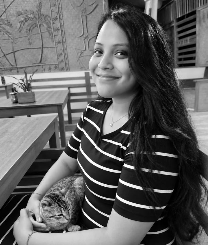 Gayatri smiling with a small tabby cat on her lap